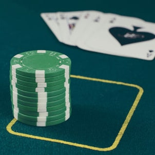 A stack of green poker chips on a green table with a set of playing cards in the background.